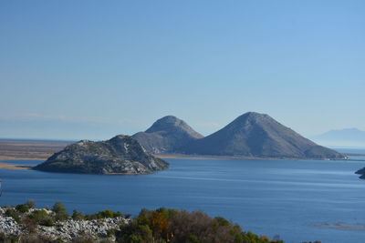 Scenic view of sea and mountains against clear blue sky