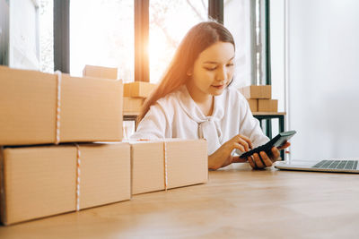 Young woman using mobile phone while sitting in box