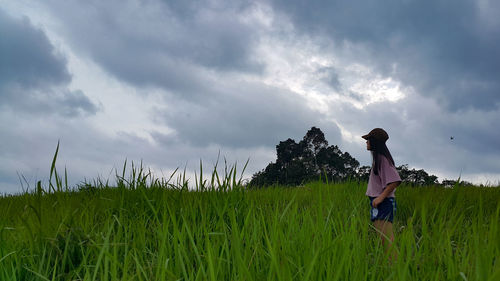 Rear view of man walking on grassy field against cloudy sky