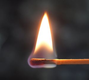 Close-up of burning matchstick against gray background