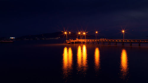 Illuminated bridge over river against sky at night