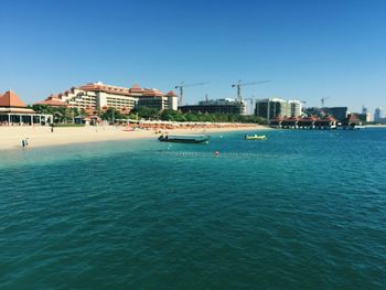 Buildings by sea against clear blue sky