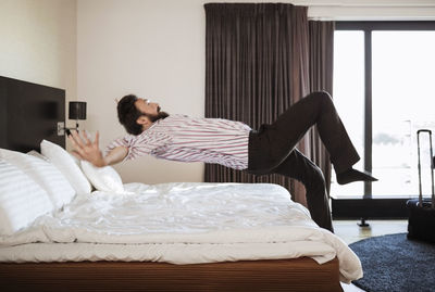 Full length of businessman jumping on bed in hotel room