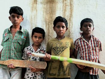 Portrait of smiling gully cricket friends standing against wall