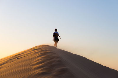 Rear view of woman walking on desert against sky