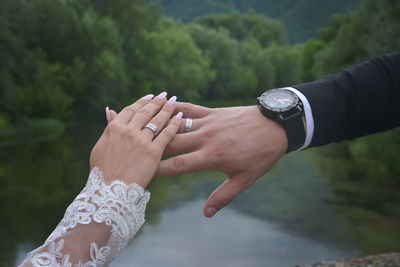 Cropped bride and groom touching by lake