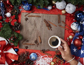 Cropped hand of man holding black coffee by spices and christmas decorations on table