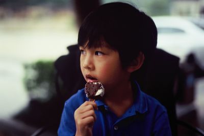 Cute boy eating ice cream while looking away outdoors