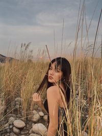 Portrait of young woman sitting on field against sky