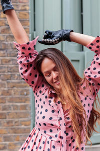 Close-up portrait of happy model in pink dress and gloves with arms in the air in london