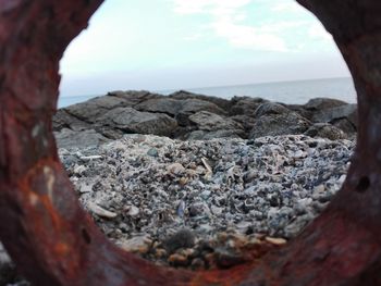 Rocky shore at sea against sky seen through rusty metal
