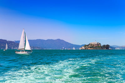 Sailboat sailing in sea against clear blue sky