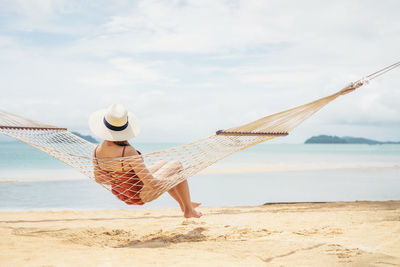 Rear view of woman sitting on hammock at beach