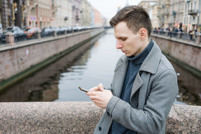 An attractive man walking across bridge in gray coat against backdrop