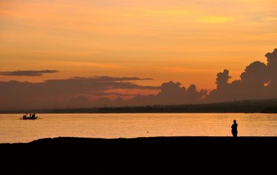 Silhouette man standing on beach against sky during sunset