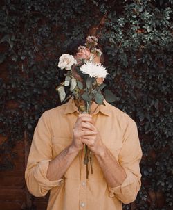 Midsection of person holding umbrella standing by flowering plant