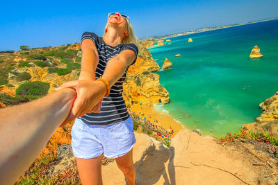 Happy woman holding cropped hand against sea