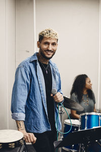 Portrait of smiling young artist holding microphone standing in classroom