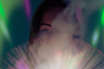 Close-up portrait of woman by illuminated lights and smoke