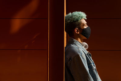 Side view of young man looking away against wall