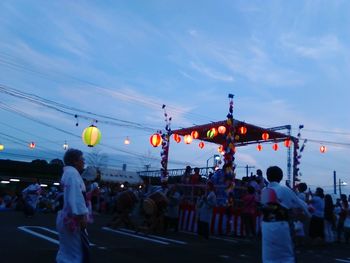 Crowd in illuminated city against blue sky