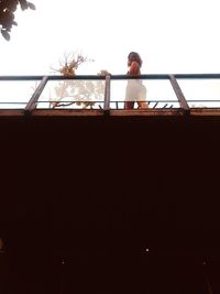 Low angle view of woman standing on railing against sky