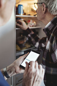 Senior woman holding smart phone standing by man in kitchen at home