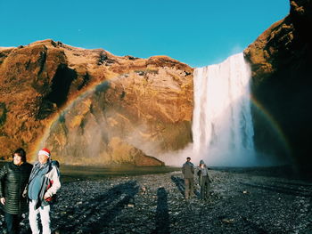 Panoramic view of people at waterfall against sky