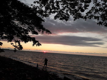 Silhouette man standing on beach against sky during sunset