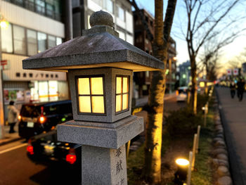 Close-up of illuminated lantern by street against buildings in city