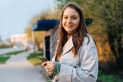 Beautiful smiling girl with long hair in a grey trench coat outdoors on the street spring