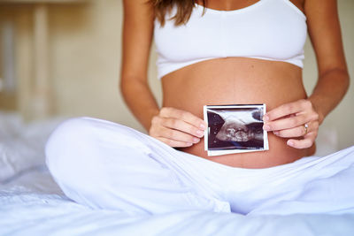 Midsection of woman using mobile phone on bed at home