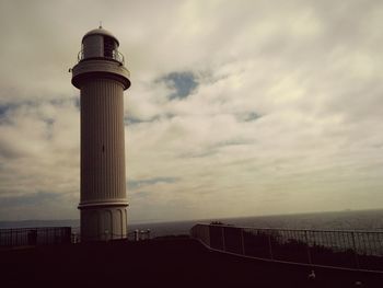 Lighthouse on sea against cloudy sky