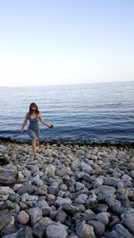 Full length of young woman standing at beach against clear sky