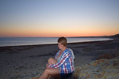 Woman sitting on beach against clear sky during sunset