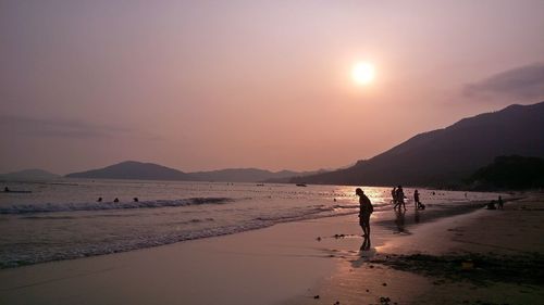 Silhouette people on beach against sky during sunset