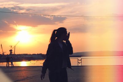 Woman standing on promenade by river against sky during sunset