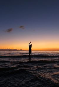 Silhouette man in sea against sky during sunset
