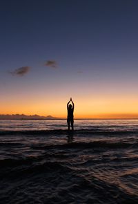 Silhouette man doing yoga at beach during sunset