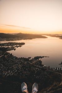 Low section of person by lake against sky during sunset