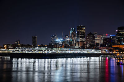 Illuminated buildings by river against clear sky at night