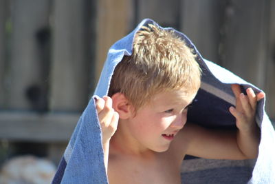 Shirtless cute boy holding towel looking away while sitting outdoors