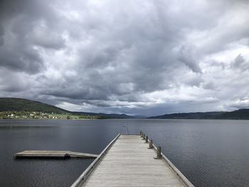 Pier over lake against cloudy sky