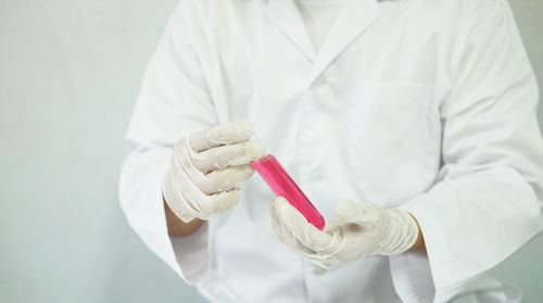 Midsection of male scientist holding test tube with pink liquid