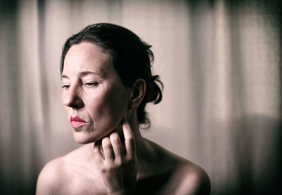 Thoughtful shirtless mature woman against curtain at home