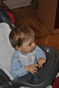 High angle view of cute boy holding spoon on baby stroller at home