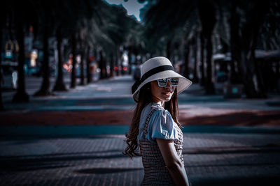 Portrait of woman with hat standing against umbrella in city