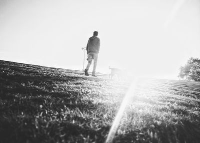 Rear view of man walking on field against clear sky