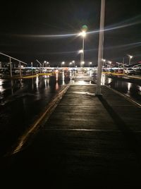 Illuminated street by river against sky at night