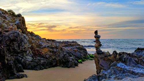 Woman on rock against sky during sunset